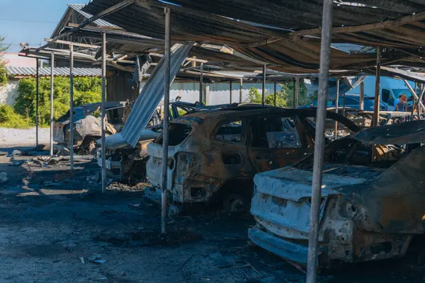 Kül ve çamur kaplı yanmış cesetlerde bükülmüş metal ve erimiş yapılar görülüyor. Arabanın içi mahvolmuş. Askeri çatışma ve bombardıman sonucu. Yıkılmış otopark.