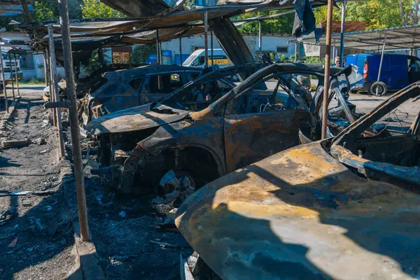 Kül ve çamur kaplı yanmış cesetlerde bükülmüş metal ve erimiş yapılar görülüyor. Arabanın içi mahvolmuş. Askeri çatışma ve bombardıman sonucu. Yıkılmış otopark.