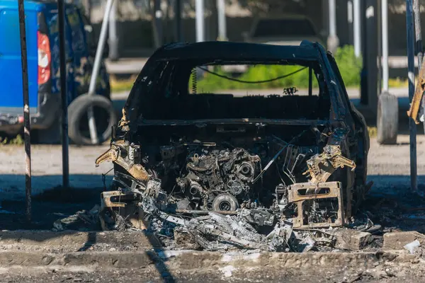 Kül ve çamur kaplı yanmış cesetlerde bükülmüş metal ve erimiş yapılar görülüyor. Arabanın içi mahvolmuş. Askeri çatışma ve bombardıman sonucu. Yıkılmış otopark.