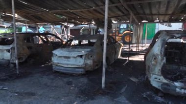 Kül ve çamur kaplı yanmış cesetlerde bükülmüş metal ve erimiş yapılar görülüyor. Arabanın içi mahvolmuş. Askeri çatışma ve bombardıman sonucu. Yıkılmış otopark.