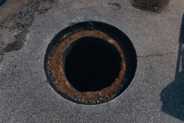 Şehir caddesinde bir iş yeri, yol yüzeyi onarımı ve rögar kapağı kurulumu. Yakın plan hazırlanmış bir delik. Resim, şehrin altyapısını korumak için yapılan çalışmaların safhalarını vurguluyor..