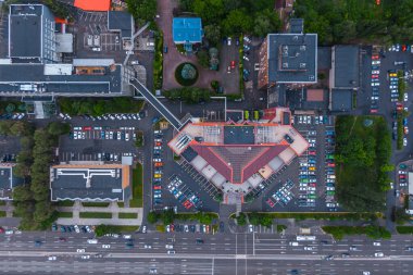 A straight-up vertical aerial photograph of a modern office or shopping center with a unique V-shaped roof. The building is surrounded by large parking lots filled with cars.