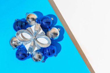 Beyaz ve mavi arka planda gümüş kurdeleli, kar taneli ve mücevherli mevcut kutudan yapılmış yaratıcı bir kompozisyon. Noel ve yeni yıl konsepti. Asgari düzeyde. Üst Manzara. Düz yatıyordu