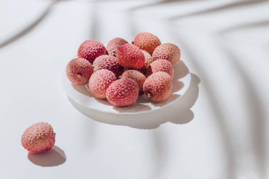 Beyaz arka planda, palmiye yaprağı gölgesiyle taze liçi meyvelerinden yapılmış en düşük tarzda kompozisyon. Yaz tatili konsepti. Durgun hayat.