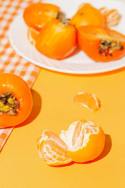 Creative layout made of orange mandarin, fresh persimmon fruits on white plate on bright background with shadow. Healthy food concept. Summer picnic idea.