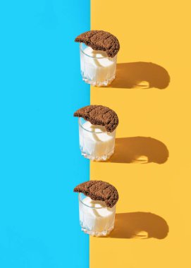 Mavi ve sarı arka planda yarım bardak kahverengi Amerikan kurabiyesi olan bir bardak sütten oluşan yaratıcı soyut kompozisyon. Asgari düzeyde. Fırın ve pasta konsepti. Kahvaltı için fikir.