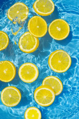 Şeffaf havuz suyundaki dilimlenmiş narenciyeden yapılmış yaratıcı bir yaz kompozisyonu. Yenileme konsepti. Sağlıklı ferahlatıcı içecek teması. Üst Manzara. Seçici odak