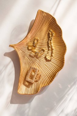 Pastel arka planda gölgeli kadın aksesuarları. Altın küpeli, bilezik ve tokalı şık kıyafetler. Moda ve güzellik konsepti