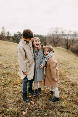 Üç çocuk, güler yüzlü, sonbahar günü parkta vakit geçiriyorlar..