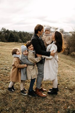 Büyük bir aile sonbahar günü dışarıda eğleniyor. Çocuklar ailelerine sarılıyor. Anne ve baba kucağında küçük kızı.