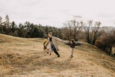 Çocuklar sonbahar günü parkta oynuyorlar, koşuyorlar ve gülüyorlar..