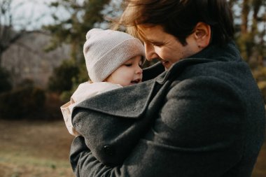 Soğuk bir sonbahar gününde küçük kızını paltosuyla ısıtan bir babanın yakın plan portresi..