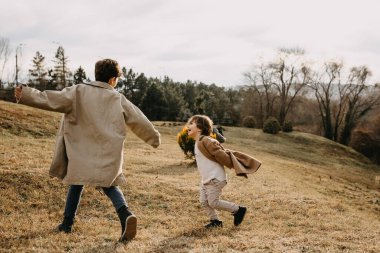 Çocuklar sonbahar günü parkta oynuyorlar, koşuyorlar ve gülüyorlar..