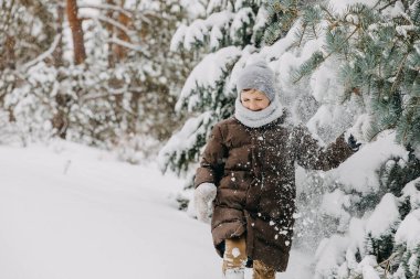 Çocuk karla kaplı büyük bir ağaç dalının altında duruyor, sallıyor..