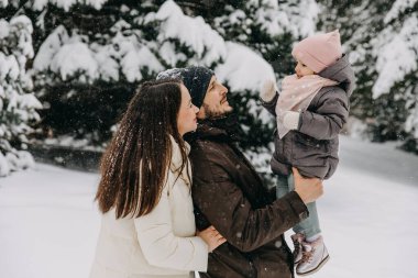 Anne ve baba, karlı bir kış gününde küçük kızıyla dışarıda oynuyorlar..