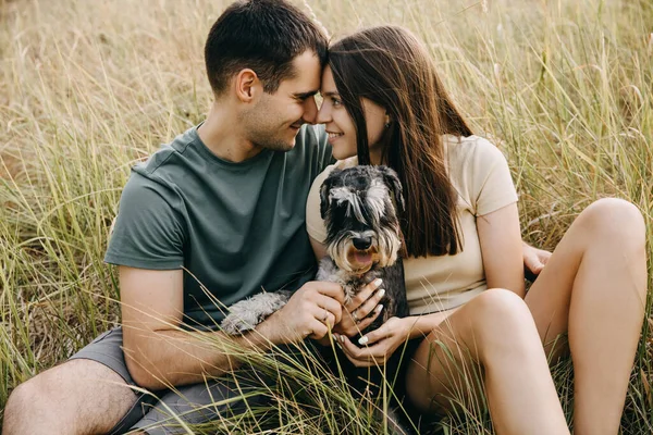 幸せなカップルの男と女の屋外に座って 小型シュノーザー純血犬を抱きかかえて 笑って — ストック写真