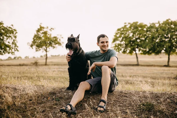 Junger Mann Sitzt Neben Einem Großen Schwarzen Hund Rasse Riesenschnauzer — Stockfoto
