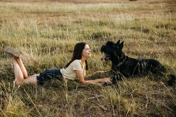 一位年轻的黑发女子躺在草地上 旁边是一只巨大的黑狗 雪纳泽品种 — 图库照片