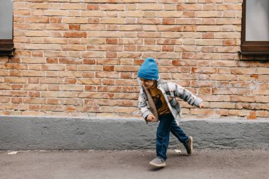 Toddler boy outdoors running on a brick wall background, on city streets.