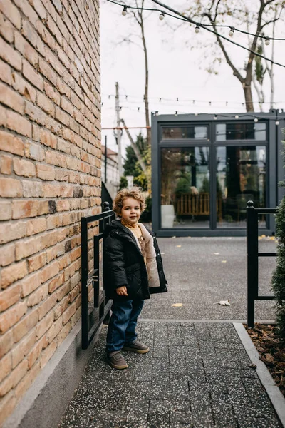 小男孩快乐地站在城市街道上 靠着砖墙 站在仁慈的花园入口 — 图库照片