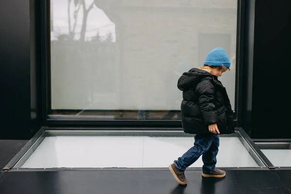 小男孩 站在城市街道上 背靠玻璃墙 — 图库照片
