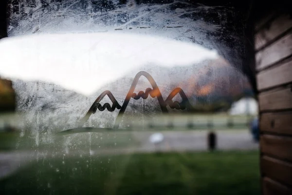 Finger drawing of three mountains on a misted window glass.