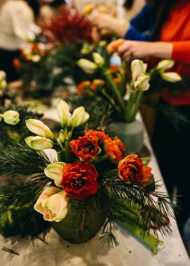 Kırmızı lale buketi, çam dalları ve amirilis. Çiçekçide çalışan kadınlar. Çiçek atölyesi kavramı.