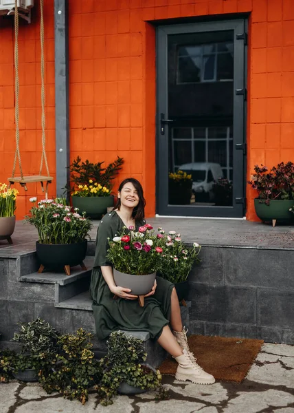 快乐的女人在一家花店的楼梯上坐着 手里拿着一个盛着兰花的大花盆 — 图库照片