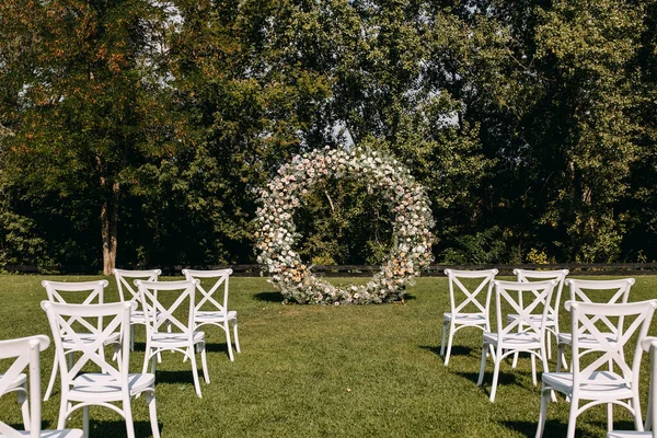Ceremonia Ślubna Okrągłym Łukiem Ozdobionym Kwiatami Białymi Drewnianymi Krzesłami Umieszczonymi — Zdjęcie stockowe