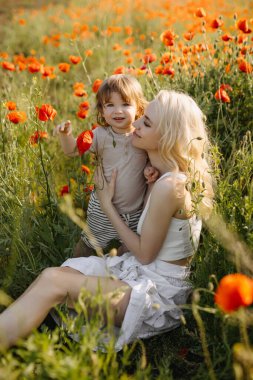 Anne ve oğlu vahşi kırmızı gelinciklerle bir tarlada oturuyor, oynuyor ve sarılıyorlar..
