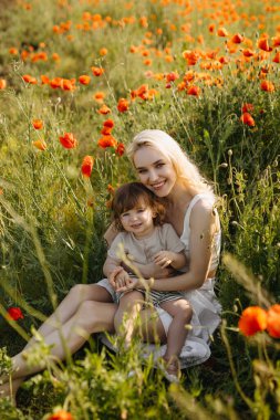 Anne ve küçük vahşi kırmızı gelinciklerle bir tarlada oturuyorlar, sarılıyorlar, kameraya bakıyorlar..
