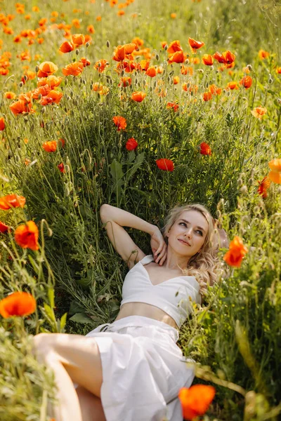 Młoda Blondynka Leżąca Polu Dzikimi Czerwonymi Makami Ubrana Białą Sukienkę — Zdjęcie stockowe
