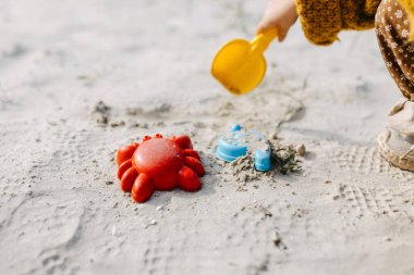 Kum kalıpları ve beyaz kumda kürekle oynayan bir çocuğun yakın çekimi.