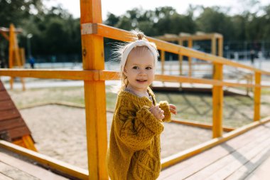 Baharda, güneşli bir günde, hardal örülü hırka giyen, oyun parkında mutlu bir kız..