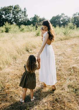 Anne iki çocukla yürüyor, el ele tutuşuyorlar, bir yaz günü bir tarlada..