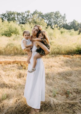 Anne iki kızını kucağında tutuyor, bir yaz günü parkta..