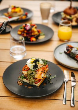 Bir tabak füme somon, guacamole ve sebzeli waffle. Brunch yemeğinin bir parçası. Kahvaltıda farklı yemeklerle dolu bir masa..