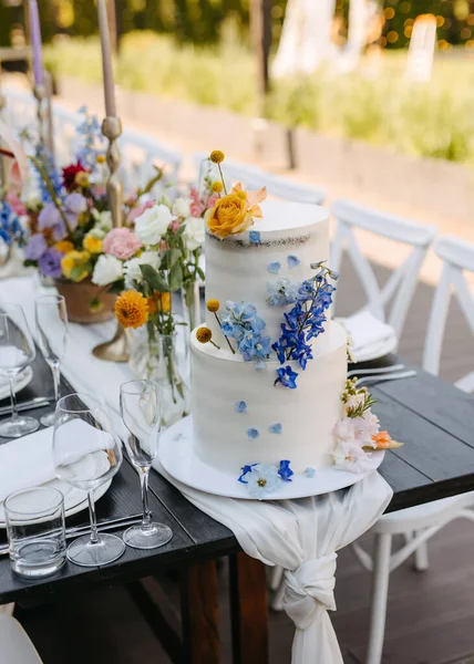 Elegant floral wedding cake on a table at an open air event.