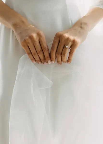 ブライダルガウンの背景に静かにベールを保持する婚約指輪を持つ女性の手 — ストック写真