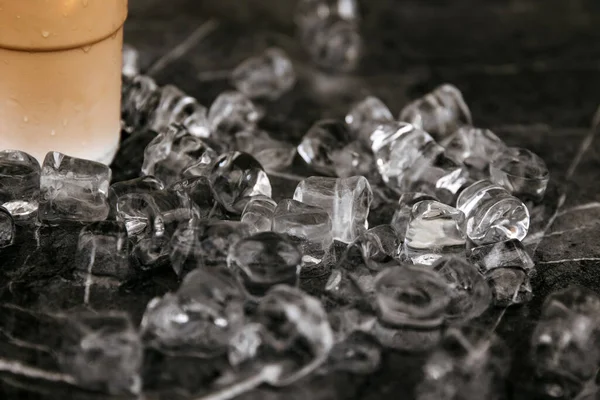 在拿铁玻璃杯旁边的黑色大理石表面上散落的冰块 — 图库照片