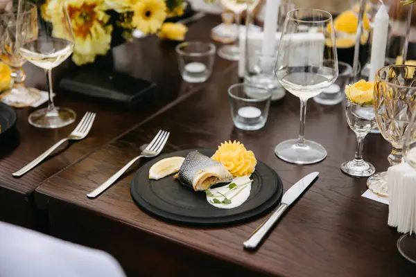 Elegant dining with fish plate, lemon, and mashed potato on black plate, yellow floral backdrop.