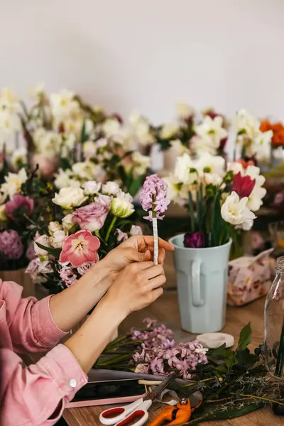 ピンクのシャツを着た人は さまざまな新鮮な花と花のデザインツールに囲まれたライラックヒヤシンスを配置します ロイヤリティフリーのストック画像