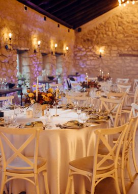 Taştan duvarlar, mum ışığında bir ortam, çiçek süslemeleri ve güzel yuvarlak masa örtüleri ve güzel yemek seti olan kırsal bir mekanda zarif bir düğün..