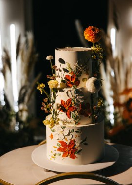 Güzel dekore edilmiş üç katlı bir düğün pastası, el boyaması çiçek tasarımları ve taze çiçeklerle..