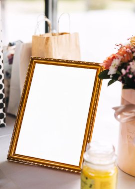 Zarif altın çerçeveli boş tabela hediye çantaları, çiçekler ve mumlarla çevrili, bir olay için sıcak ve davetkar bir ortam yaratıyor..