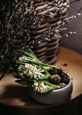 Söğüt dallarının yanındaki gri bir kasede beyaz sümbüllerin yakın çekimi.