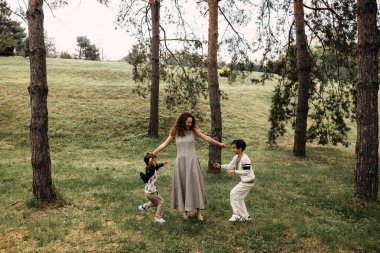 Anne ve oğulları bir orman açıklığında neşeyle oynuyorlar. Çocuklar annenize doğru koşuyor..