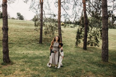 Mutlu anne iki oğluyla güneşli bir orman çayırında yürüyor..