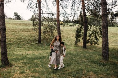 Mutlu anne iki oğluyla güneşli bir orman çayırında yürüyor..