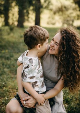 Gülümseyen anne, açık havada küçük oğluna sevgiyle bakıyor.